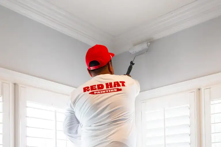 A Red Hat painter rolling a ceiling in a bright room